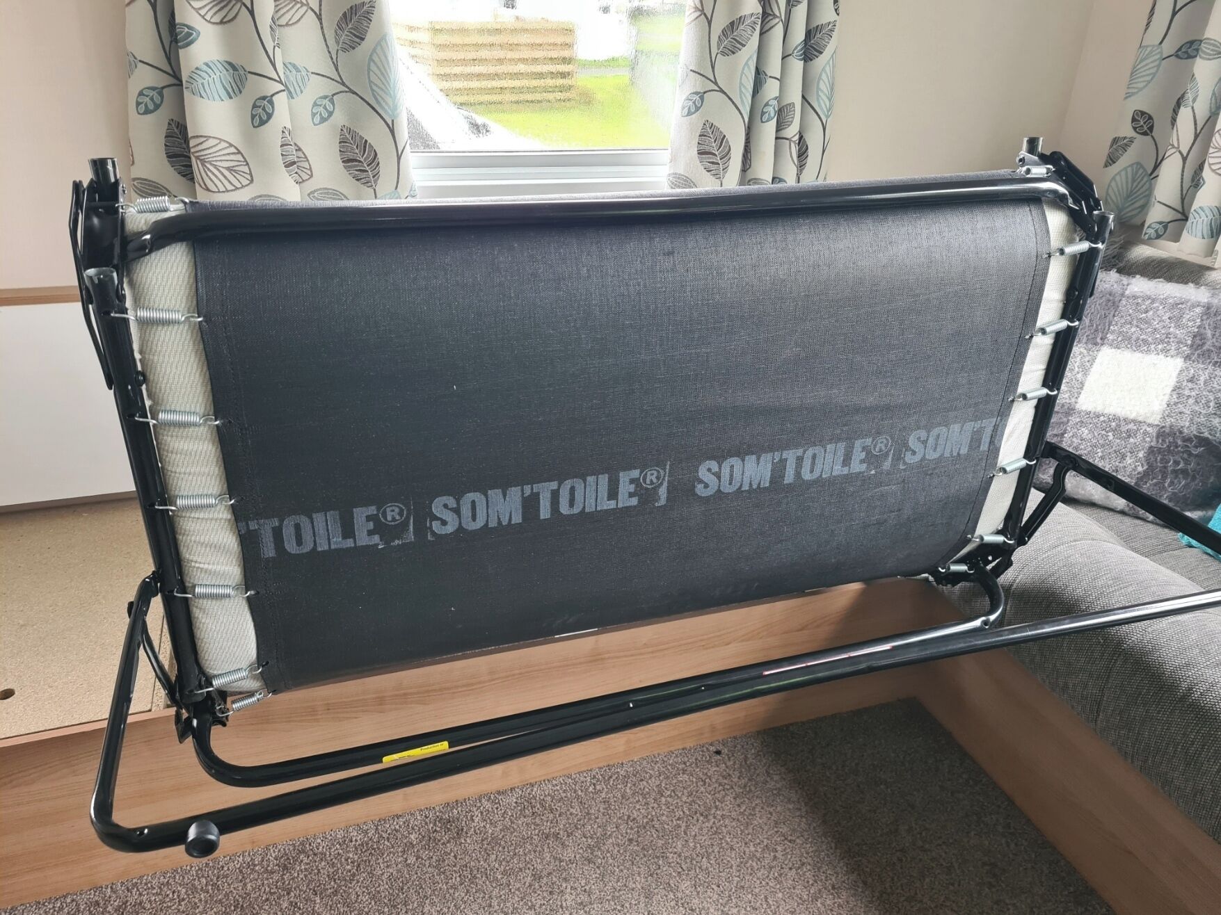 A chair with a black cushion and metal frame, positioned in a room with a window and curtains.