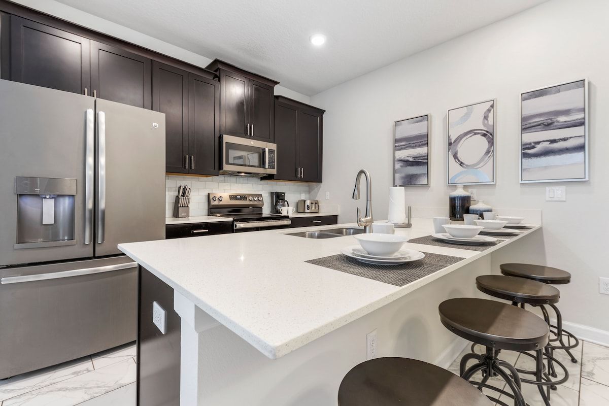 A modern kitchen with dark cabinets, stainless appliances, a white island, and bar stools.