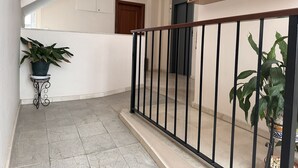 A hallway with a black metal railing, a potted plant on a small table, and a wooden storage unit above the railing.