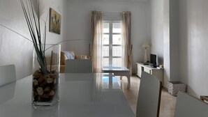 A modern, well-lit room with a dining table, chairs, a TV, and a window with curtains.
