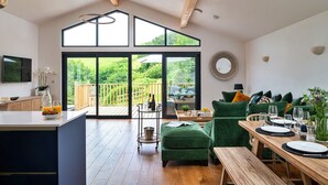 Een ruime woonkamer met een houten plafond, grote ramen en een schuifpui die leidt naar een balkon.
