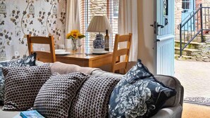 Una sala de estar acogedora con un sofá, dos sillones, una mesa con un jarrón de girasoles y una ventana con persianas.