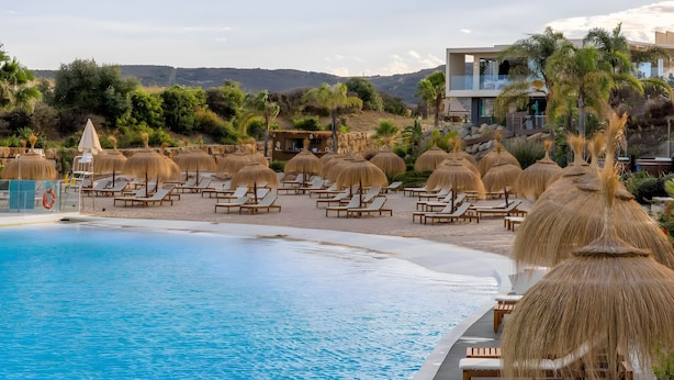A poolside area with lounge chairs and umbrellas, a pool, and a building with a balcony overlooking the landscape.