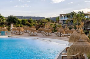A poolside area with lounge chairs and umbrellas, a pool, and a building with a balcony overlooking the landscape.