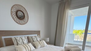 A neatly made bed with white linens, a patterned throw blanket, and rolled towels.