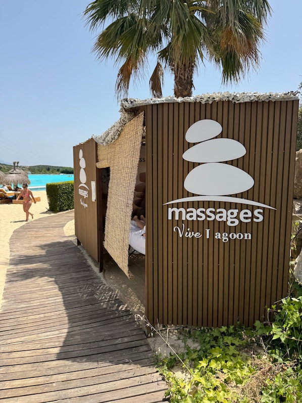 A wooden massage hut with a sign reading 'masses Vive I agoon' on a wooden deck.