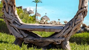 A heart-shaped wooden sculpture with a view of a clear blue sea and distant boats.