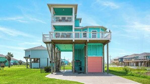 A multi-story building with a balcony, a garage, and a grassy area in front. - Steps to the Beach | Tiki Bar Fun | Epic Bay Views | Sleeps 8 | Pet-Friendly (Crystal Beach)