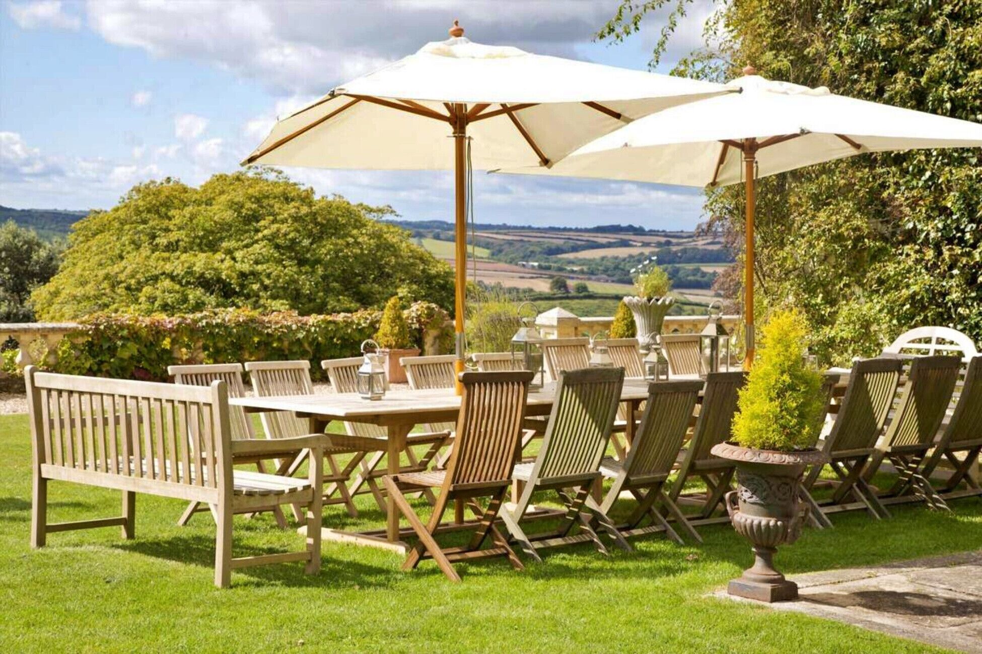 An outdoor dining area with wooden furniture and white umbrellas, overlooking a scenic landscape.