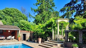 En swimmingpool med trappsteg som leder upp till en pergola, omgiven av frodig grönska.