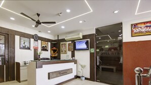 A hotel reception area with a reception desk, a clock, a ceiling fan, a television, and a framed picture on the wall. - RTS HOTEL & Spa (New Delhi)