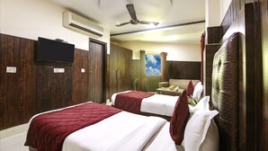 A hotel room with two beds, a ceiling fan, an air conditioning unit, a television, and a window with a view of the sky. - RTS HOTEL & Spa (New Delhi)