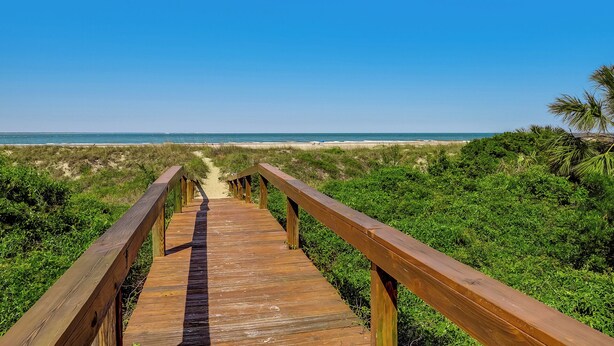 A wooden boardwalk leading to a beach with clear skies.