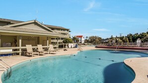 A pool area with lounge chairs and a building with a balcony.