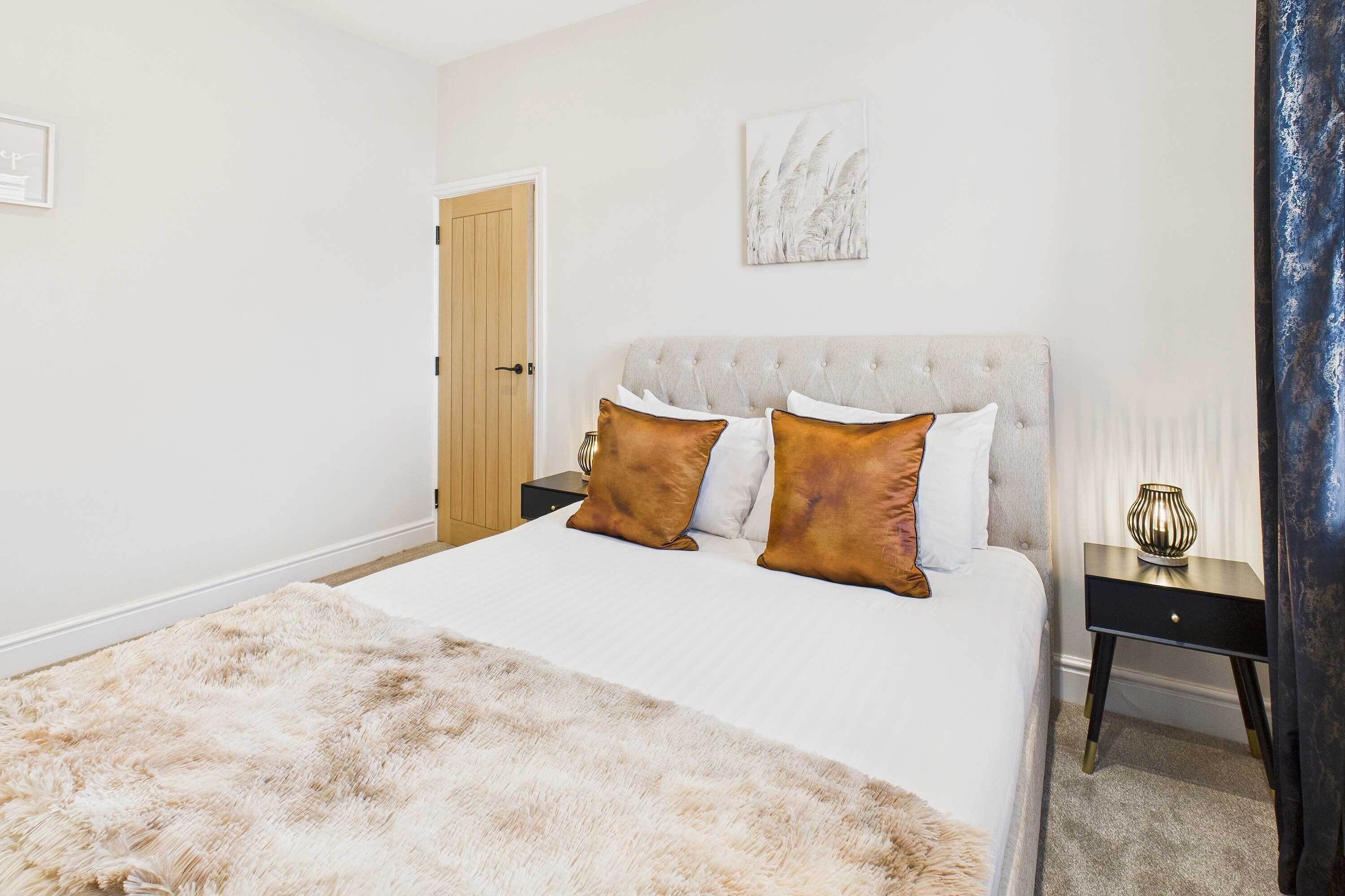 A bedroom with a large bed, a nightstand, a door, and a wall-mounted artwork.