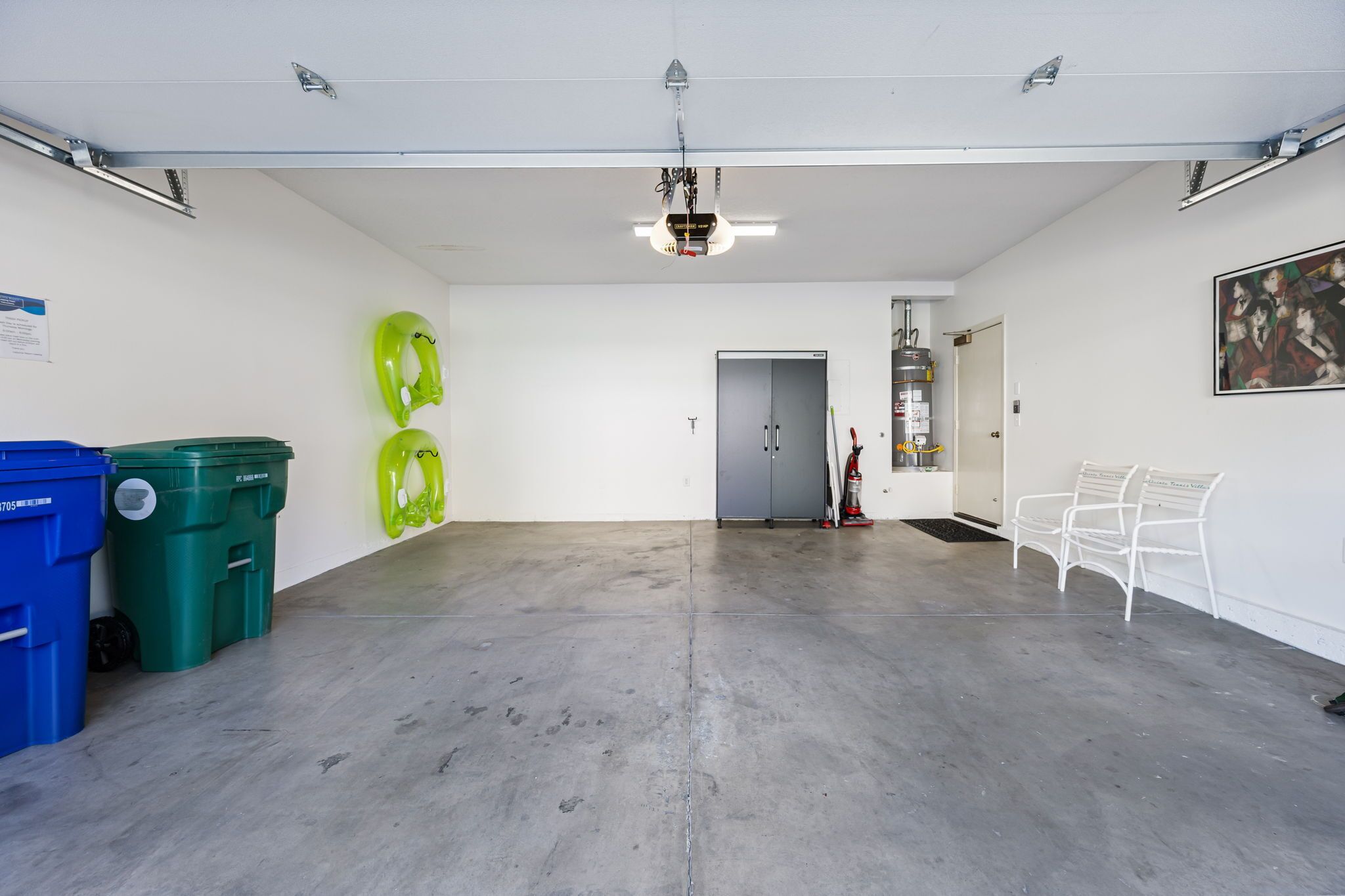 Amplio espacio interior con buena iluminación, suelo de concreto, botes de reciclaje verde y azul, un banco blanco y una puerta que da a otra habitación.