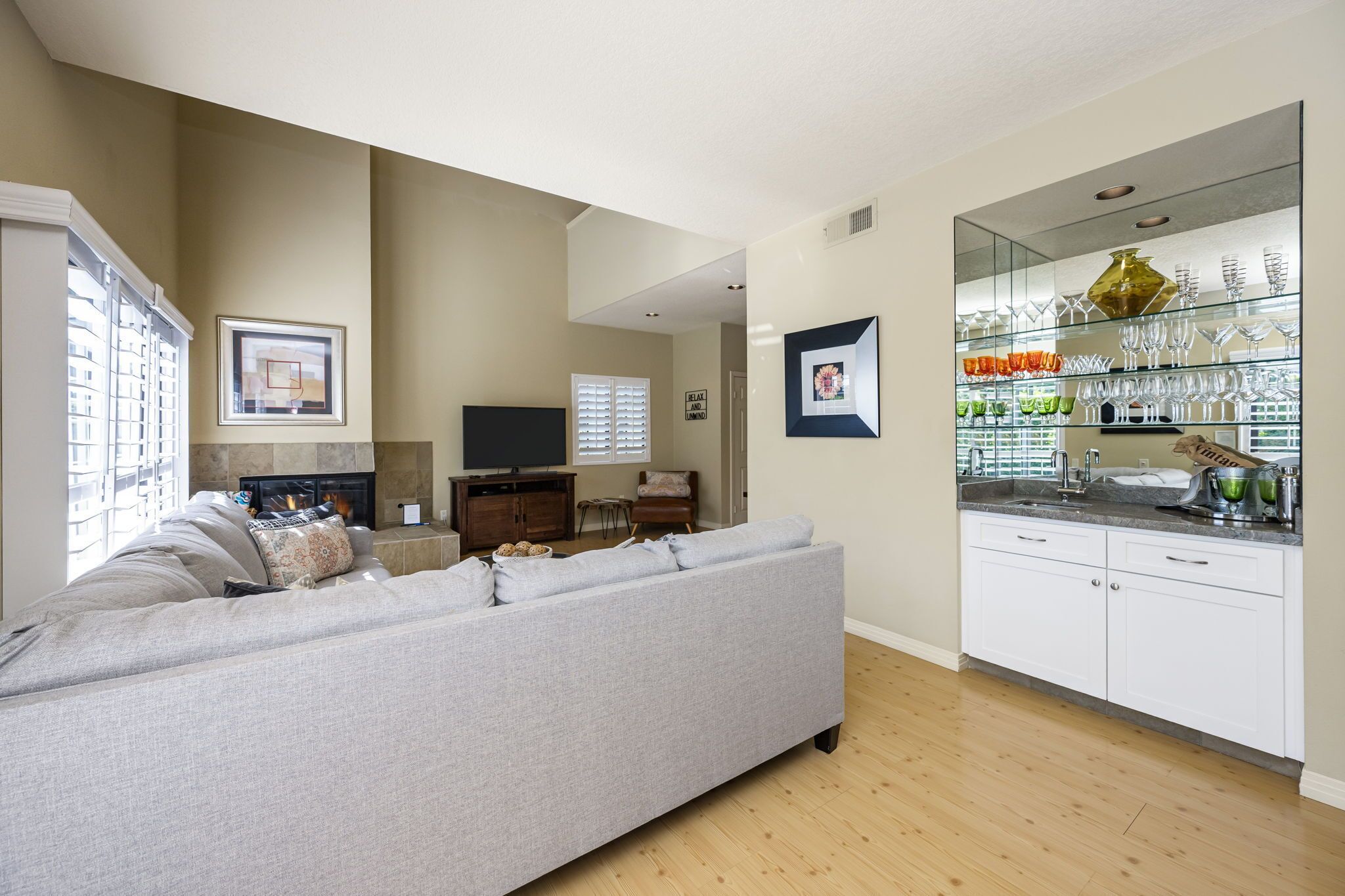 A living room with a grey sofa, a TV, and a fireplace. There is a kitchen area with a countertop and cabinets.