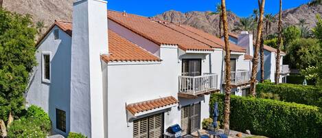 A white building with a red-tiled roof, a balcony, and a patio area with outdoor furniture.