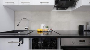 A modern kitchen with white cabinets, a black countertop, a built-in dishwasher, and a coffee maker.