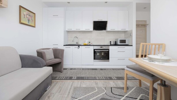 A modern kitchen with white cabinets, a microwave, and an oven. There is a dining table with chairs and a small rug on the floor.