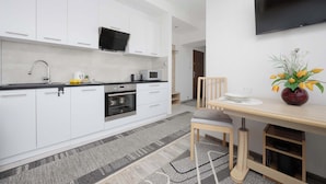 A modern kitchen with white cabinets, a microwave, and a stove. There is a dining table with chairs and a vase of flowers.