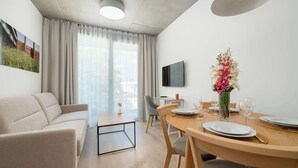 Una sala de estar moderna con un sofá, una mesa de comedor, sillas, un televisor y un centro de mesa con flores.