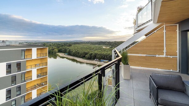 A modern apartment with a balcony overlooking a river and greenery.