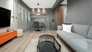 A modern living room with a grey sofa, orange side table, and a glass coffee table.