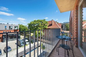 Un balcon avec une table et des chaises, une vue sur la rue et un immeuble à la façade en briques rouges.