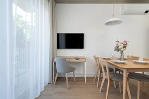 Un espace repas moderne avec un téléviseur à écran plat fixé au mur, une table à manger en bois pour quatre personnes et une chaise rembourrée de couleur grise.