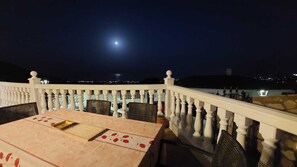 Ein Balkon mit Tisch und Stühlen, einem Geländer und einem Nachthimmel mit Mond.