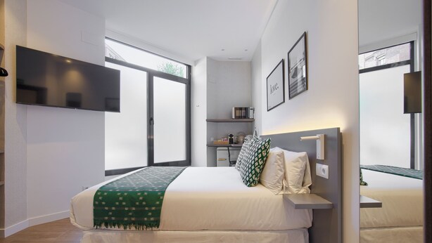 Quarto moderno com cama grande, televisão de tela plana na parede, mesa de cabeceira e janela com vista.