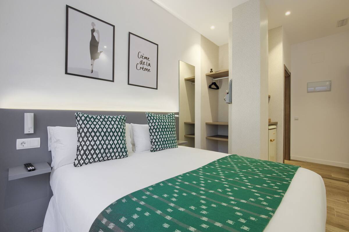 A neatly made bed with patterned pillows, a green blanket, and two framed pictures on the wall.