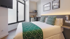 Quarto de hotel com cama, escrivaninha, cadeira, micro-ondas e janela.