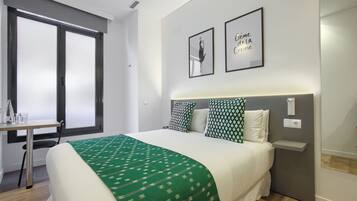 Hotelkamer met een bed, bureau en stoel. Twee ingelijste foto's hangen aan de muur, een raam en een nachtkastje.