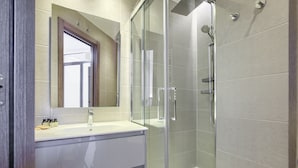 Casa de banho moderna com chuveiro fechado por vidro, lavatório branco e espelho sobre a toucador.