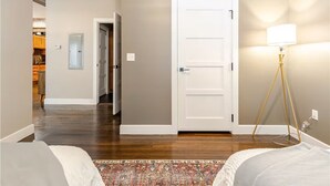Une chambre d’hôtel avec un plancher en bois, une porte blanche, un tapis à motifs et une lampe de chevet.