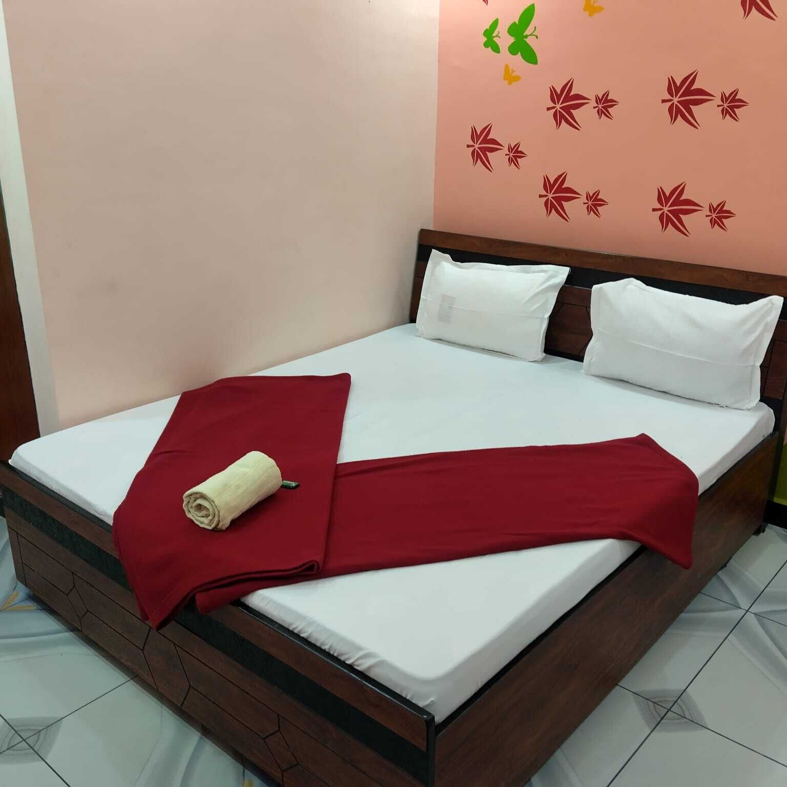 A bed with white bedding, a red blanket, and a rolled towel.