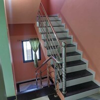 A staircase with metal railings and a handrail, leading to a landing with a window and a curtain.
