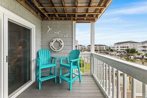 A balcony with two turquoise Adirondack chairs and a small table, overlooking a marina with boats and buildings in the background.