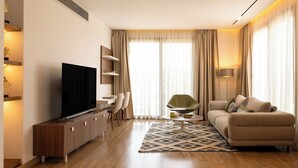 Ein modernes Wohnzimmer mit Flachbildfernseher, einer Couch, einem Essbereich mit Stühlen und einem gemusterten Teppich.