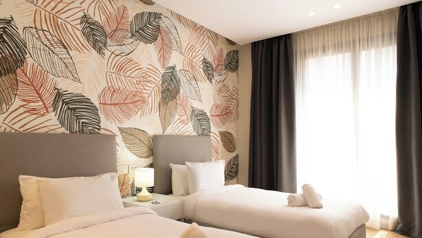 Ein Hotelzimmer mit zwei Betten, einem Nachttisch mit Lampe und einem großen Fenster mit Vorhängen.