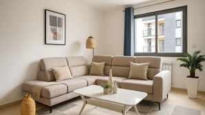 Un saló modern amb un sofà seccional beix, una taula de centre blanca i una finestra gran amb cortines blaves.