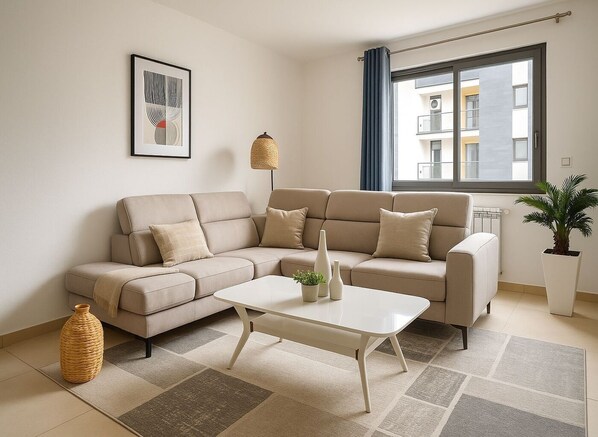 A modern living room with a beige sectional sofa, a white coffee table, and a large window with blue curtains.