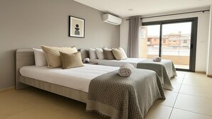 Una habitació d'hotel amb dos llits, roba de llit beix, un quadre al mur i una finestra gran amb vista a edificis.