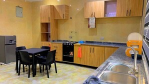 A kitchen with wooden cabinets, a granite countertop, a sink, and a dining area with chairs. - DFW Abodes Luxury Home (Akure)