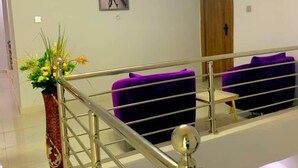 A modern interior with a staircase, a purple sofa, and a wall-mounted sign reading "DE ROYALE". - DFW Abodes Luxury Home (Akure)