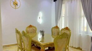 A dining area with a round table and six chairs, a wall clock, and a ceiling light fixture. - DFW Abodes Luxury Home (Akure)
