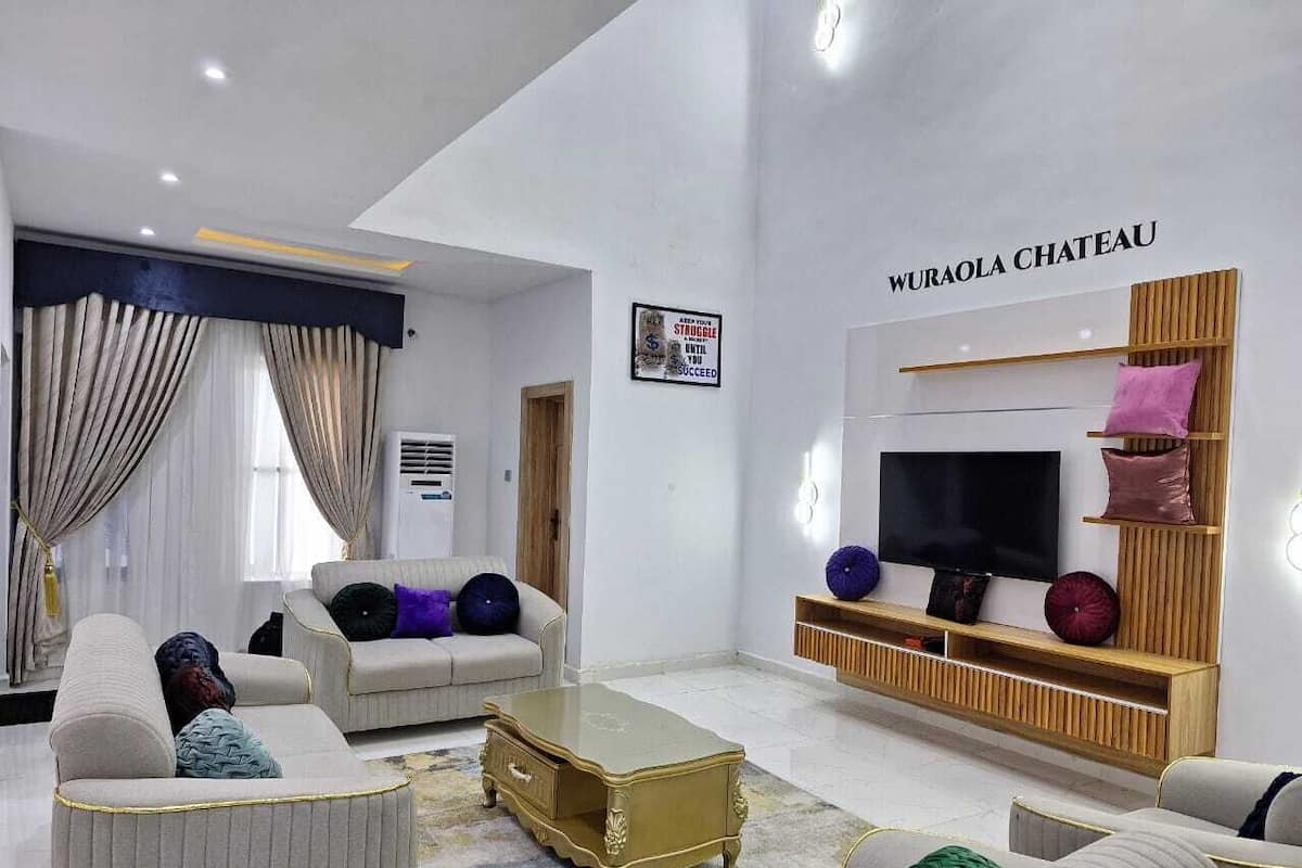 A modern living room with a large TV, comfortable seating, and a sign reading "Wuraola Chateau".