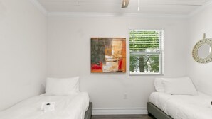 Une chambre avec deux lits, une grande peinture abstraite, une fenêtre avec des stores et un miroir décoratif.